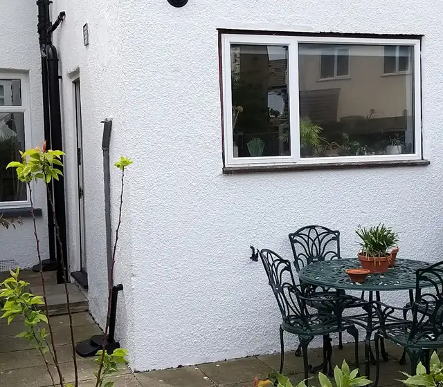 Rear wall of a house in fresh white masonry paint beside a patio