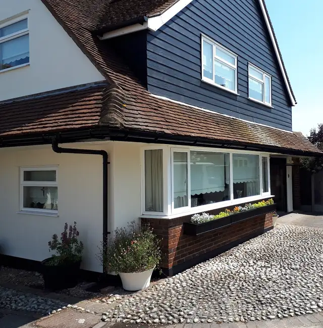 House with navy painted weatherboarding above cream render and a brick plinth